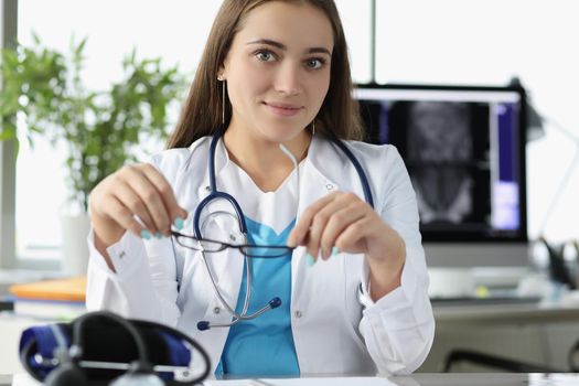 Portrait of young woman doctor sit in office at work in hospital. Intern wait for patient on appointment wear stethoscope tool. Healthcare, help concept