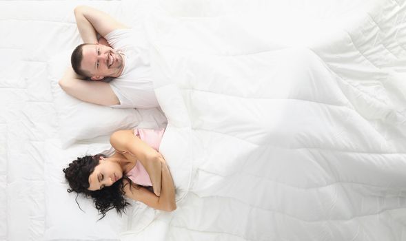 Top view of wife and husband happily laying bed, white bedclothes. Wake up and start new day, good morning. Comfort, relaxation, family, sweet home concept