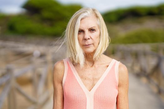Beautiful mature female walking along a wooden path near the beach., wearing a nice orange dress. Elderly woman enjoying her retirement at a seaside retreat.