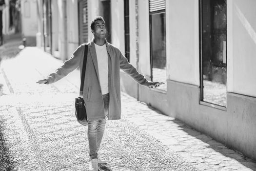 Young black man walking down the street carrying a briefcase and a smartphone. Cuban guy in urban background.