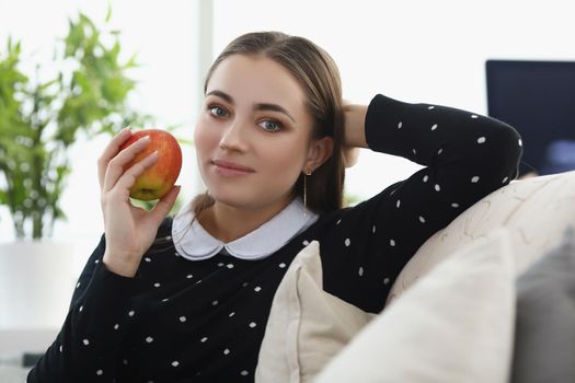 Portrait of pretty young woman sit comfy on couch at home, fresh apple fruit as snack. Lovely girl having lunch. Chill, relaxation, weekend fun concept
