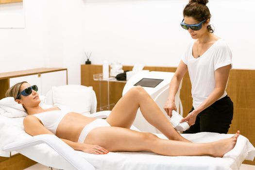 Beautiful woman receiving legs laser hair removal at a beauty center.