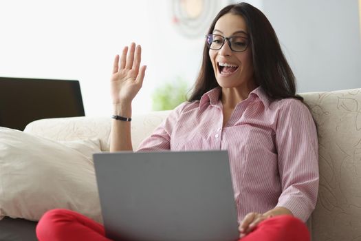 Portrait of pretty young woman wave hello show gesture online on laptop. Talk to friend or family on video call. Technology, greeting, happiness concept