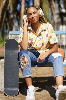 Young smiling African woman with skateboard Mixed-race girl relaxing after riding skateboard listening to the music outdoors.