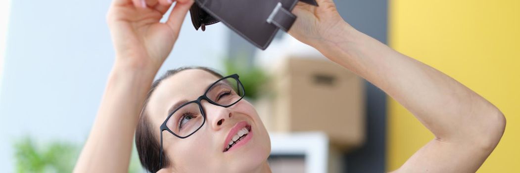 Young woman with glasses looking into empty leather wallet. Global economic crisis concept