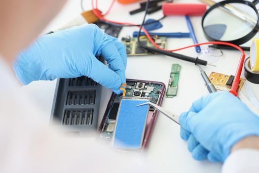 Close-up of person fixing broken mobile phone model, put new battery inside, return old cellphone to life. Workplace full with tools. Handyman, fix concept