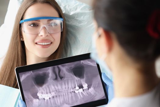 Portrait of patient on dental consultation in clinic, doctor examine teeth x ray on digital tablet device. Stomatologist on appointment. Teethcare concept