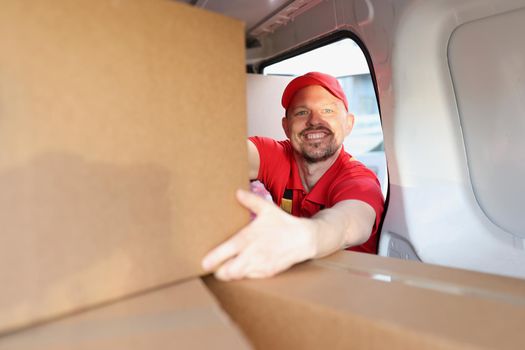Portrait of man enjoying working in delivery company, put boxes in truck for further delivery on address. Happy man help with relocation. Handyman concept
