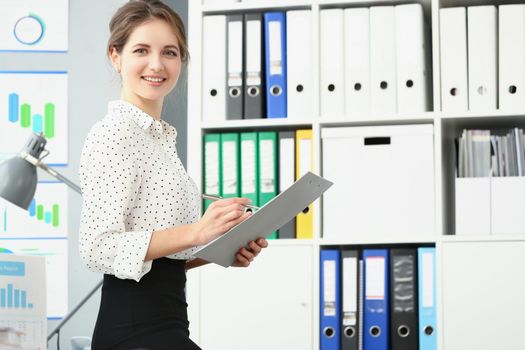 Portrait of smiling employee woman posing in conference room, making notes on paper. Businesswoman report on business meeting in company. Biz firm concept