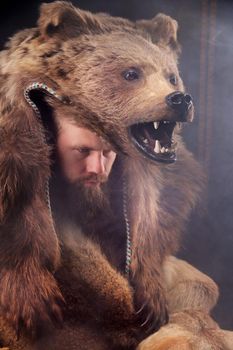 Bearded Scandinavian shaman with a bear skin on his head. Caucasian man dressed in animal skins pensively looks to the side.