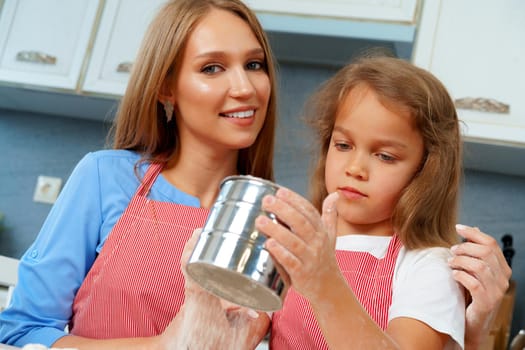 Mother and her little daughter preparing dough in kitchen close up