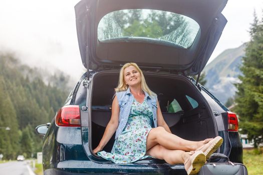 Woman with car near countryside road through mountain Alps.