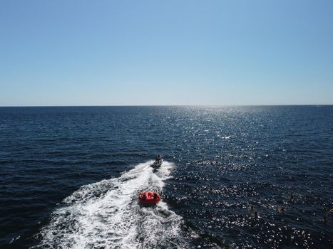 Inflatable attraction. Happy people are going to swim on an air mattress behind a jet ski. Tourists ride the inflatable watercraft boat. Jet ski skating people on a large Inflatable raft