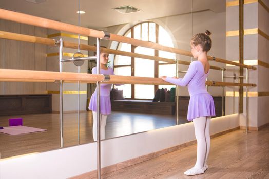 little girl wear pointe in ballet class near frame and large mirror