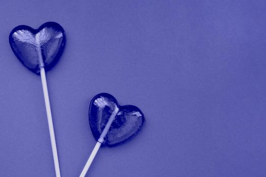Purple lollipops in the form of hearts on a purple background. The concept of Valentine's Day. Demonstrating the colors of 2022 - Very Peri.