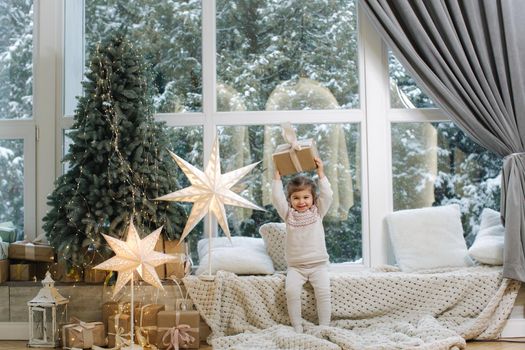 Happy beautiful girl take present in front of big window. Christmas time. It's snow outside. Christmas tree.