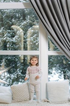 Happy beautiful girl take present in front of big window. Christmas time. It's snow outside. Christmas tree.