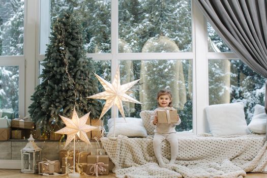 Happy beautiful girl take present in front of big window. Christmas time. It's snow outside. Christmas tree.