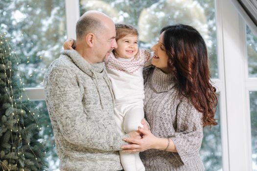 Gradparents hug her granddaughter near fir tree at home. Christmas mood of happy people.