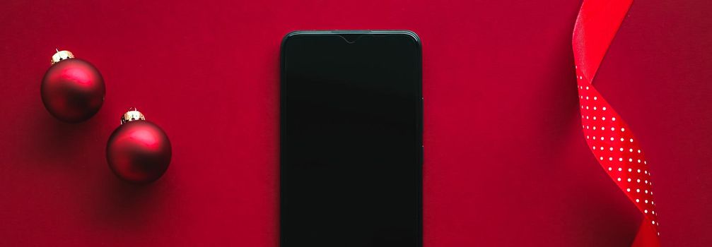 Christmas phone app and holiday message concept. Smartphone with blank black screen and xmas decoration on red background as flat lay mockup design.