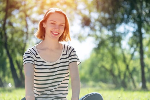 Portrait of a young attractive woman. Sitting cross-legged in the park