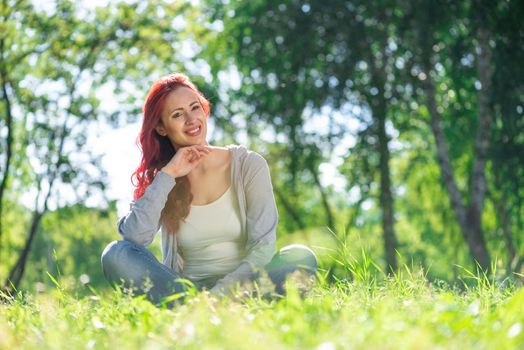 Portrait of a young attractive woman. Sitting cross-legged in the park