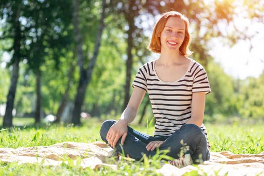 Portrait of a young attractive woman. Sitting cross-legged in the park