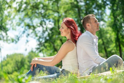 Young couple sits in the park with their backs to each other. Spending time with loved ones