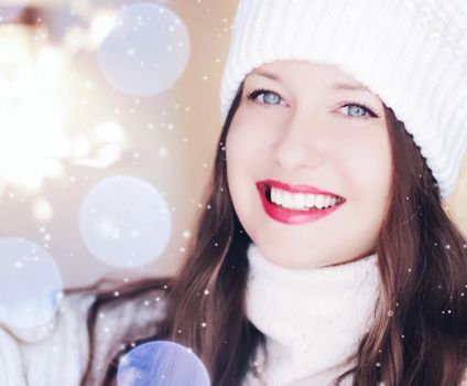 Christmas, people and winter holiday concept. Happy smiling woman wearing white knitted hat as closeup face xmas portrait, snow glitter and bokeh effect.