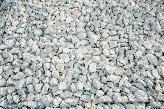 strengthening the slope with stones behind the wire. grey texture. construction. Granite stones behind a metal grate