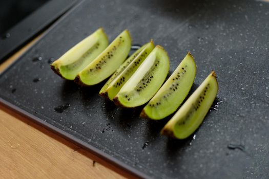 Green kiwi wedges on black kitchen cutting board, close-up. Kiwifruit fresh. Seasoning and serving ideas for fruits