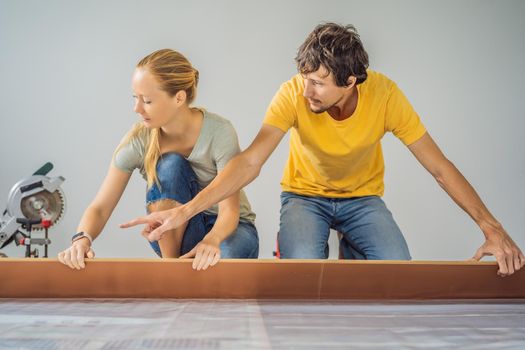 Married couple installing new wooden laminate flooring on a warm film floor. Infrared floor heating system under laminate floor.