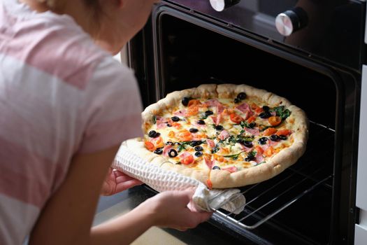 A woman takes homemade pizza with sausages out of the oven, close-up. Traditional Italian recipe, lockdown