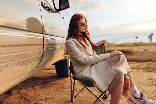 beautiful woman sitting on a chair in a field wearing dark glasses near the car endless field. High quality photo