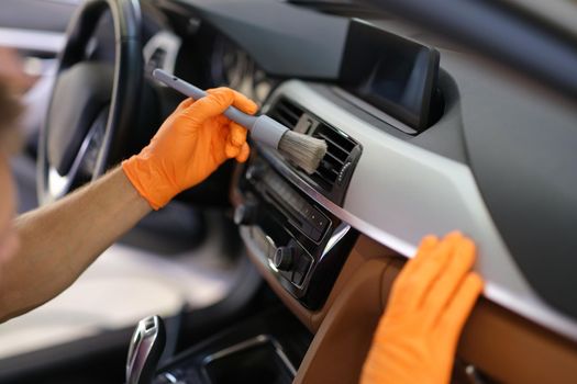 Hands in gloves with a dust brush, close-up. Cleaning between the vents in the machine. Car interior cleaning