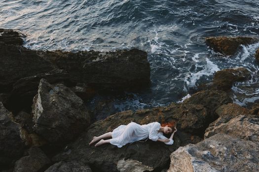 attractive woman with long hair lying on rocky coast with cracks on rocky surface nature landscape. High quality photo