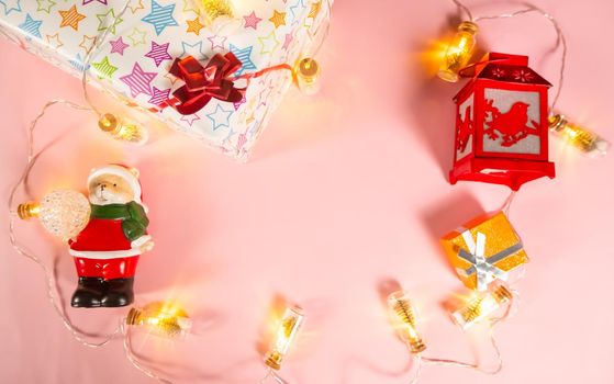Christmas background - Christmas decorations - a garland, a gift box, a flashlight and a bear in a Santa Claus costume on a light pink background, copy the space. High quality photo