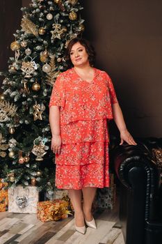 a woman in a red dress standing next to a Christmas tree in an interior decorated for celebrating Christmas and New Year.