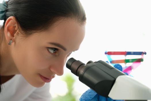 Beautiful woman looks through a microscope, profile view, close-up. DNA research, genetics. Chemical analysis of cells