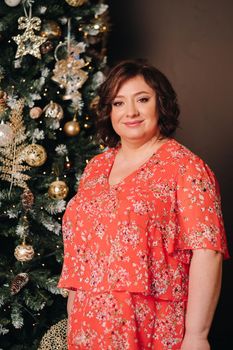 a woman in a red dress standing next to a Christmas tree in an interior decorated for celebrating Christmas and New Year.