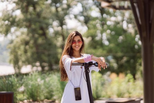 Young beautiful woman and electric scooter in the park, modern girl, new generation, electric transport, ecological transport