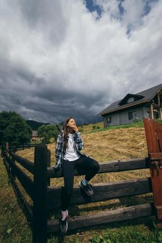 A young attractive Caucasian female sitting on a fence and posing at camera