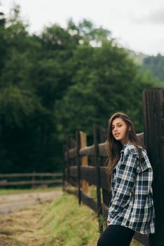 A young attractive Caucasian female stand by a fence and posing at camera