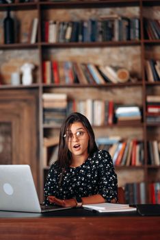 Young beautiful woman in glasses works at the laptop while sitting at the table