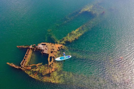 Woman on paddle board, sup next to Abandoned broken shipwreck sticking out of the sea.