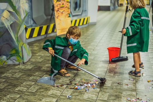 A boy in a working uniform and a medical mask sweeps the floor. Coronovirus COVID 19 concept.