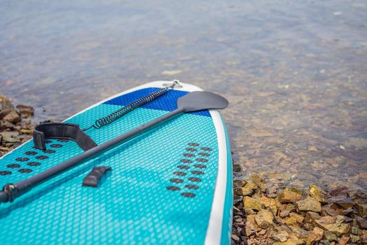 Blue sapboard with paddle and black pump lying on the shore.