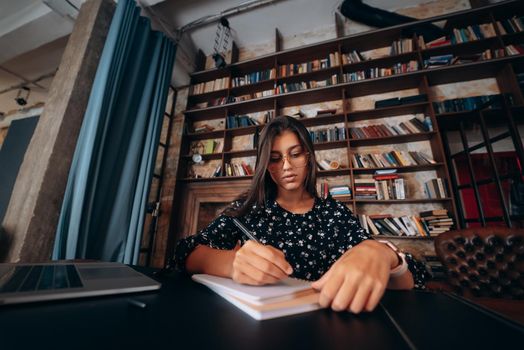 A woman's hand writing down on a white blank notebook on table.