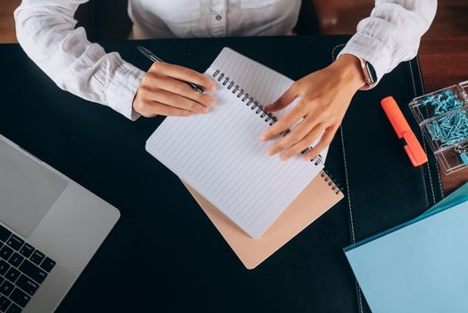 A woman's hand writing down on a white blank notebook on table.