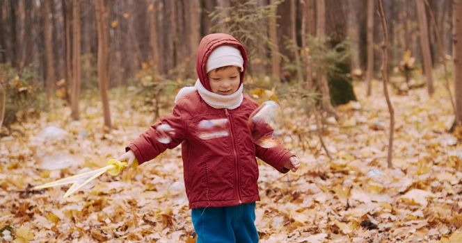 Little, a cute girl blowing soap bubbles in an autumn park. The concept of a holiday, birthday, healthy lifestyle and family weekend